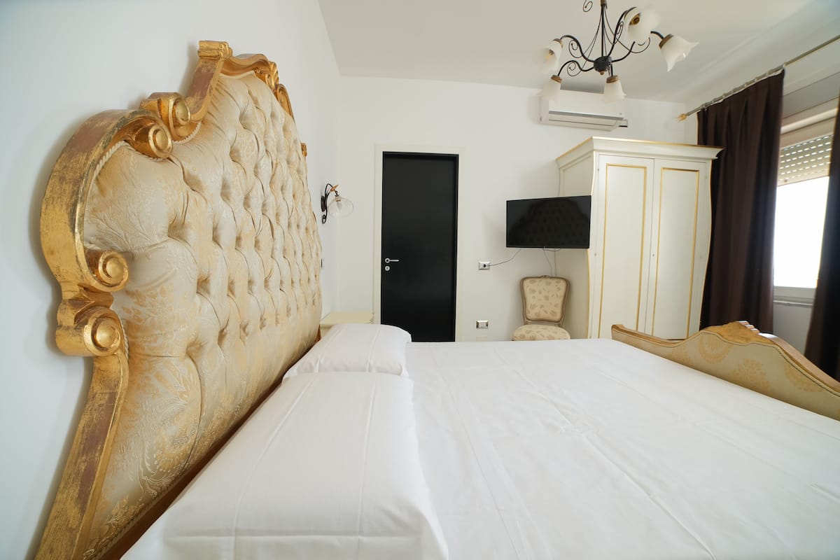 A hotel room with a large bed, a wardrobe, a television, and a chandelier.