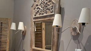 A bathroom with a round sink, a mirror with an ornate frame, two wall-mounted lamps, and a towel on the counter. - Les Jardins de la Tour (Chatillon-sur-Chalaronne)