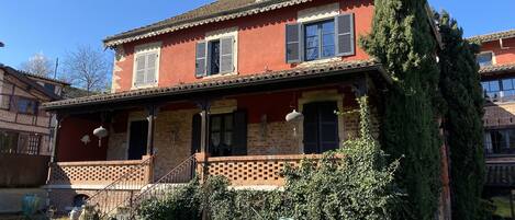 A two-story house with a red facade, a tiled roof, and a small balcony.