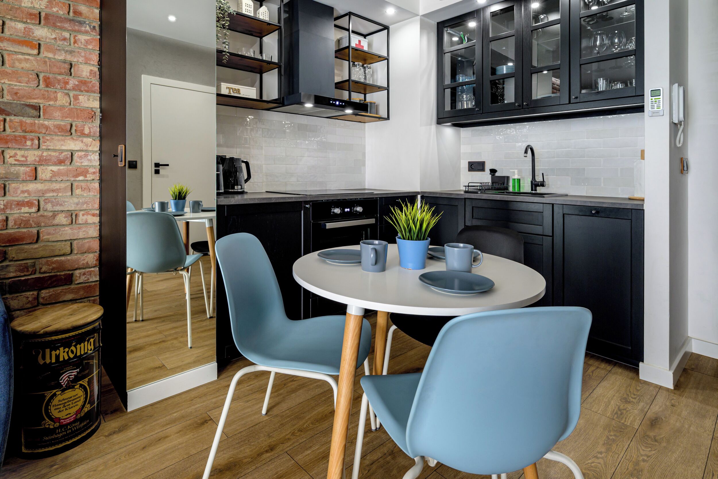 A modern kitchen with black cabinets, a white countertop, and a round table with blue chairs.