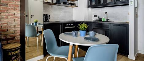 A modern kitchen with black cabinets, a white countertop, and a round table with blue chairs.