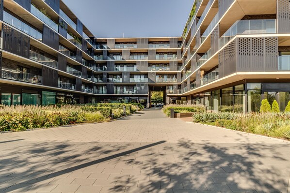 Un immeuble moderne à plusieurs étages, doté de balcons, d’une cour intérieure et d’une façade combinant verre et métal.