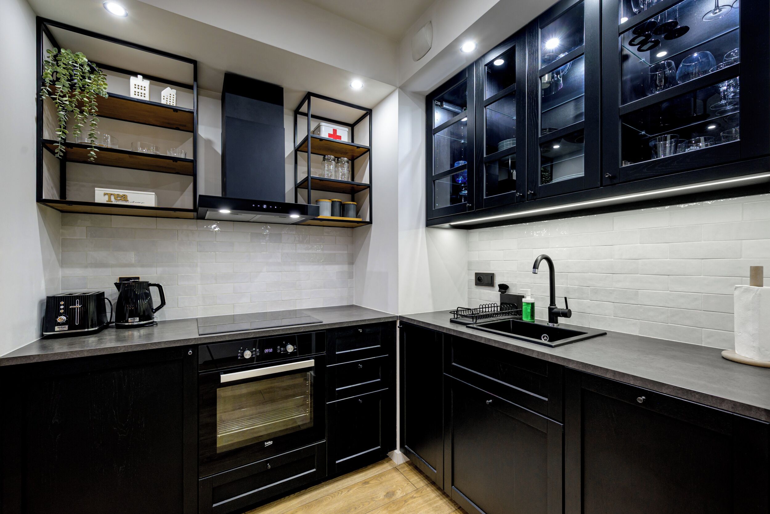 Una cocina moderna con armarios negros, horno empotrado, cafetera y un lavabo con grifo.