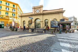 Un edificio histórico con una torre de reloj, ventanas en arco y una plaza empedrada.