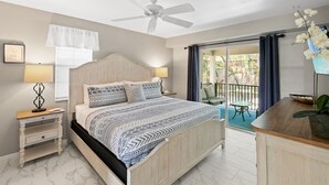 Un dormitorio con cama, mesitas de noche, ventilador de techo, ventana con cortinas y vistas a un espacio exterior.