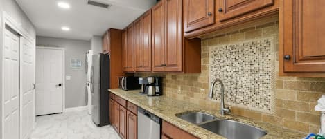 A kitchen with wooden cabinets, a granite countertop, a sink, and a tiled backsplash.