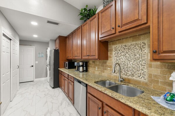 Cocina con armarios de madera, encimera de granito, pileta y salpicadero de azulejos.