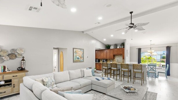 Una sala moderna con un sofá modular, un comedor con taburetes altos y una cocina con alacenas de madera.