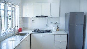 A kitchen with white cabinets, a stainless steel refrigerator, a gas stove, and a window with decorative bars. - Captivating 3-bed Apartment in Lagos (Lekki)