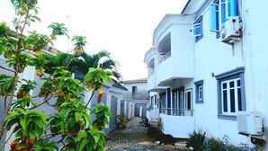 A narrow street with white buildings, a cobblestone path, and greenery. - Captivating 3-bed Apartment in Lagos (Lekki)