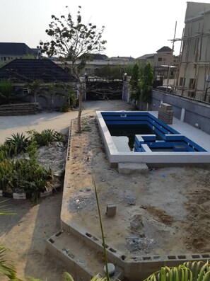 Un chantier de construction avec une piscine en cours de construction, des structures en béton environnantes et un arbre.