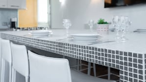 A modern kitchen with a tiled backsplash, white chairs, and a dining table set with plates, glasses, and a small plant. - Italianway Comfort - Torino 57 B (Milan)