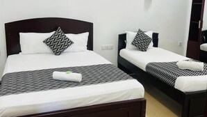 Two single beds with dark wooden frames and white bedding, a wall-mounted light fixture, and a painting above the beds. - Blue Diamond Resort (Trincomalee)