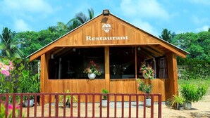 A wooden building labeled "Restaurant" with a pitched roof, large windows, and potted plants. - Blue Diamond Resort (Trincomalee)
