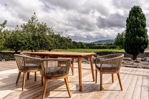 Een houten terras met een tafel en stoelen, omgeven door groen en een stenen muur.