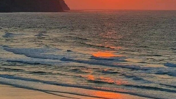 Ein Sonnenuntergang über dem Meer mit Wellen und einer entfernten Küstenlinie.