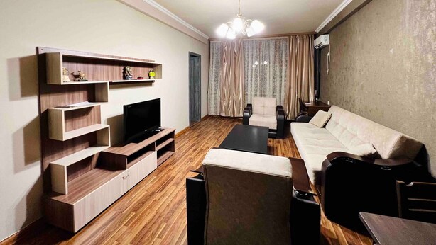 Una sala de estar moderna con un sofá, televisor, mueble de entretenimiento de madera y un comedor.