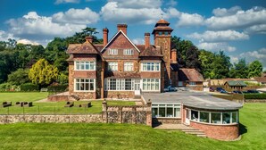 A large, historic house with multiple chimneys, a conservatory, and a well-maintained lawn. - Meadow 2 Bedroom Lodge 1 (Umberleigh)