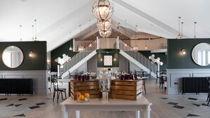 A spacious hotel lobby with a high ceiling, a central staircase, and a dining area with wooden tables and chairs. - Meadow 2 Bedroom Lodge 1 (Umberleigh)