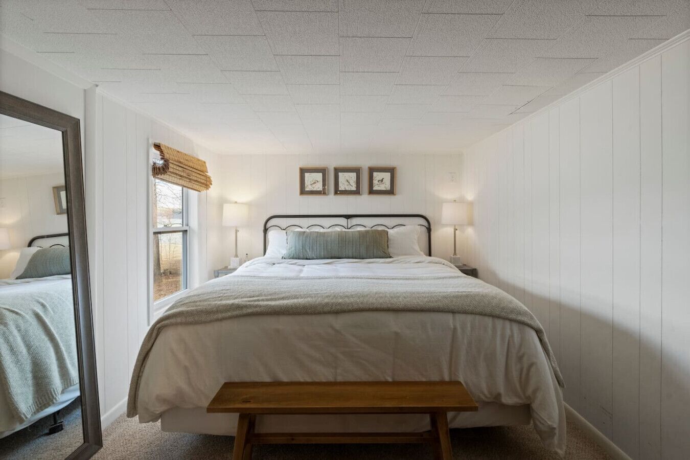 Un dormitorio con cama, lámparas de noche, un banco de madera y ventana con vistas.
