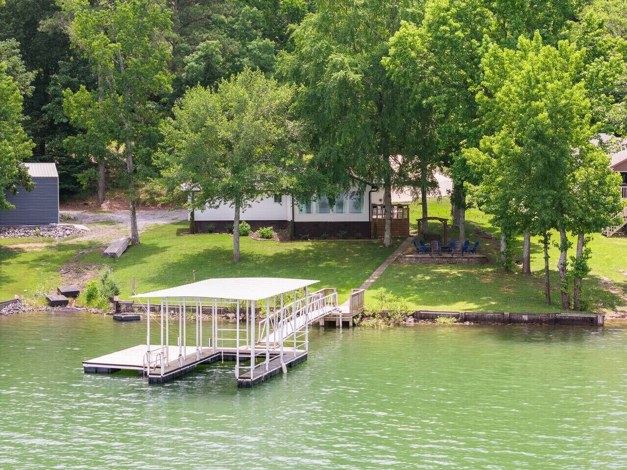 A dock extending into a lake with a covered seating area and a grassy area with a gazebo in the background.