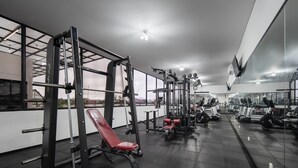 Ein Fitnessraum mit verschiedenen Trainingsgeräten, darunter eine Hantelbank, ein Squat-Gestell und Laufbänder.