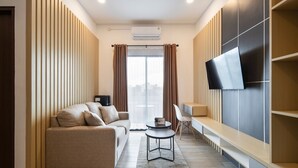 Ein modernes Wohnzimmer mit einer Couch, einem kleinen Tisch, einem an der Wand befestigten Fernseher und Blick auf die Stadt durch große Fenster.
