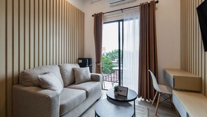 Ein modernes Wohnzimmer mit einer Couch, einem kleinen runden Tisch, einem Fernseher und einem Balkon mit Vorhängen.