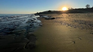 Una playa con el sol poniéndose en el horizonte, olas tranquilas y cielo despejado.