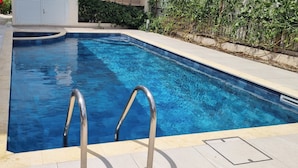 Una piscina rectangular con agua cristalina azul, rodeada por un suelo de baldosas y un muro de piedra.