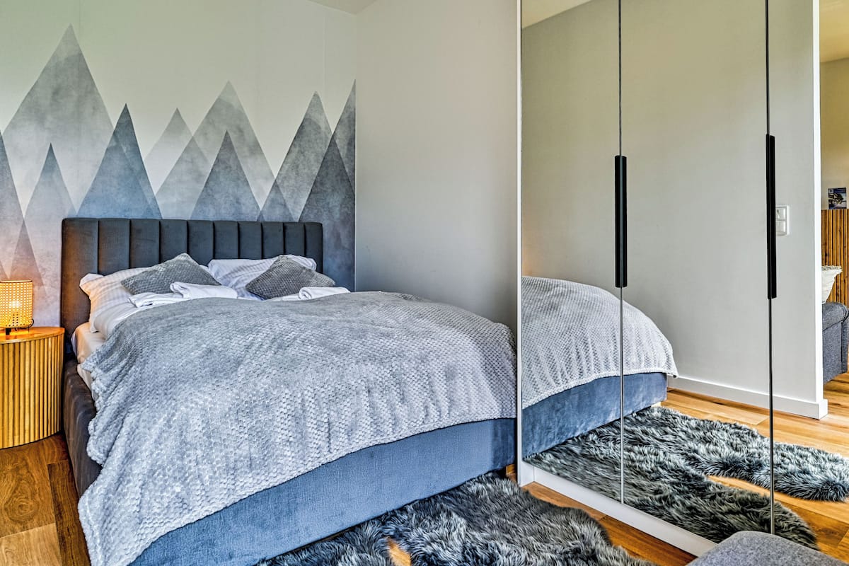 A modern bedroom with a bed, a nightstand, a wall-mounted lamp, a fur rug, and a wardrobe.