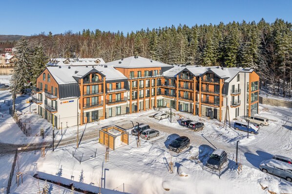 A modern multi-story hotel with a central courtyard, surrounded by snow-covered trees and a clear sky. - Apartamenty Sun & Snow Ostoja Parku Narodowego (Szklarska Poreba)