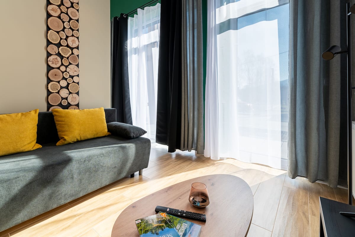 A modern living room with a grey sofa, yellow cushions, a coffee table, and a large window with sheer curtains.