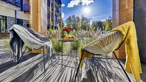 A wooden deck with two chairs, one with a grey towel and the other with a yellow towel. A small table with a fruit bowl and flowers is in the center. - Apartamenty Sun & Snow Ostoja Parku Narodowego (Szklarska Poreba)