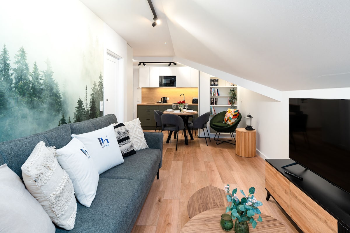 A modern living room with a grey sofa, a flat-screen TV, and a dining area with a wooden table and chairs.