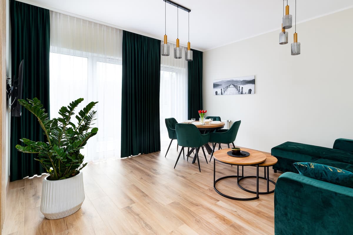 A modern living room with a green sofa, a dining table with chairs, and a potted plant.
