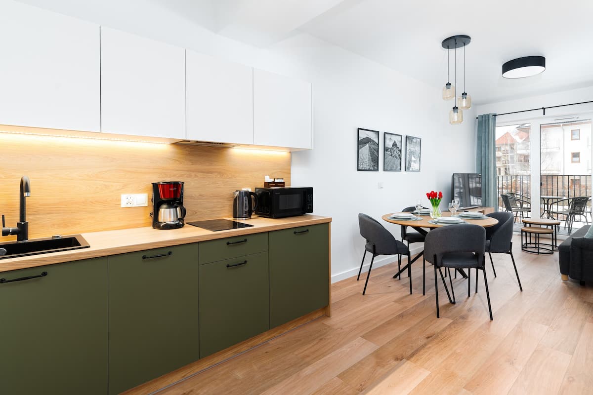 A modern kitchen with a wooden countertop, green cabinets, and a dining area with a table set for two.