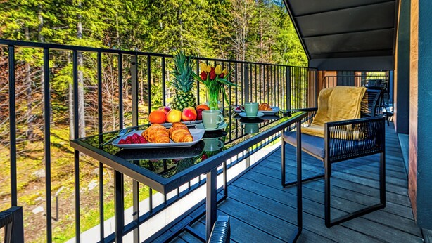 A balcony with a breakfast setup including croissants, fruits, and a vase of flowers.