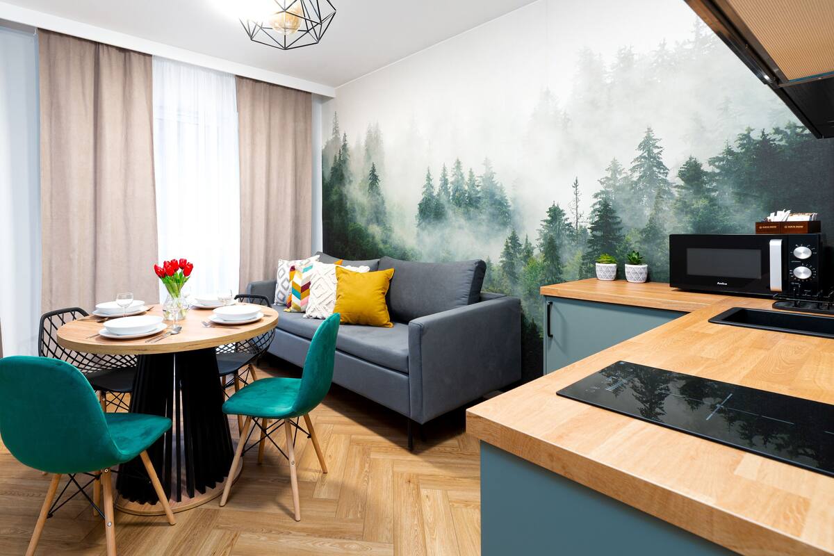 A modern kitchen with a microwave, a dining area with a table set for two, and a grey sofa.