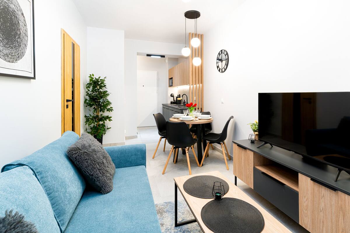 A modern living room with a blue sofa, a TV, and a dining area with a wooden table and chairs.