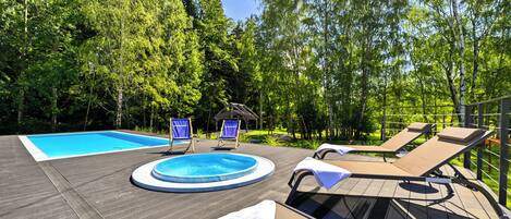 A wooden deck with a swimming pool, lounge chairs, and a small gazebo.