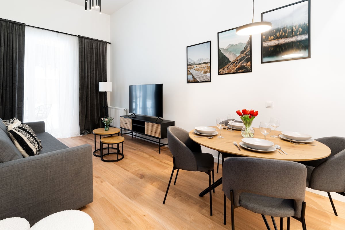 A modern living room with a sofa, a dining table set for two, and a flat-screen TV.