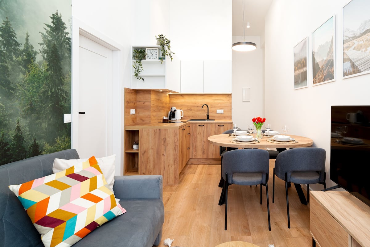 A compact living space with a kitchen, dining area, and a sofa with a colorful pillow.
