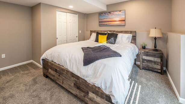 A bedroom with a wooden bed frame, a white bedspread, and a gray carpet. - Luxury Meets Convenience *** Four Beds, Three Full Baths*** (Smithville)