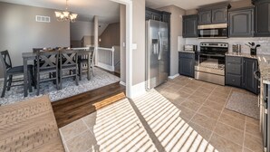 A modern kitchen with dark cabinets, stainless steel appliances, and a dining area with a wooden table and chairs. - Luxury Meets Convenience *** Four Beds, Three Full Baths*** (Smithville)