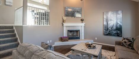 A living room with a fireplace, a ceiling fan, and a large painting on the wall.