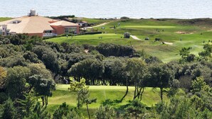 Ein Golfplatz mit Clubhaus, Bäumen und einem Gewässer im Hintergrund.