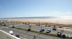 A coastal road with a beach view, parking spaces, and a clear sky.