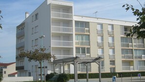 Ein mehrstöckiges Wohngebäude mit Balkonen, einer überdachten Außenbereich-Sitzgelegenheit und blauem Himmel.