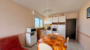 Eine kleine Küche mit Mikrowelle, Backofen und Spüle, ein Esstisch mit gemustertem Tischläufer und ein rotes Sofa.